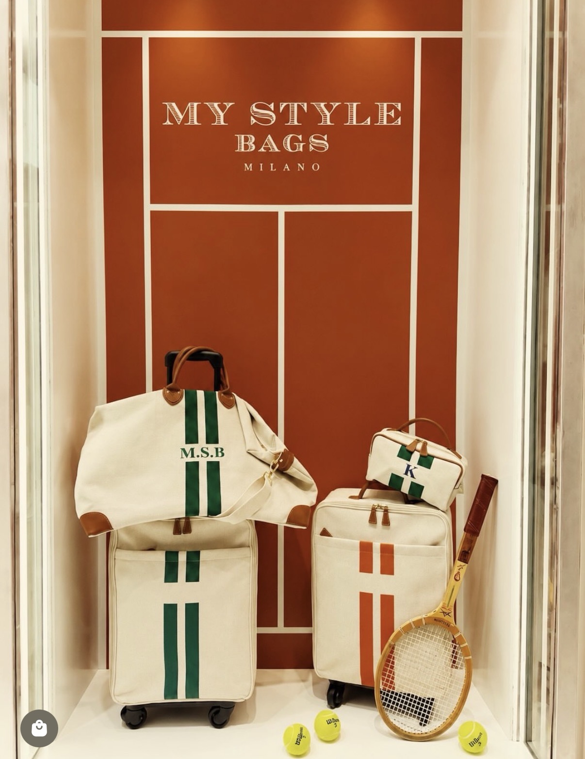 Travel bags and a vintage racket before a clay-court backdrop